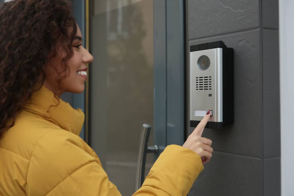 Home young african american woman ringing intercom with camera near building entrance